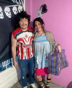 a man and woman standing next to each other in front of a pink wall with skulls on it