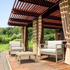 two chairs and a table on a wooden deck under a pergolated roof with stone pillars