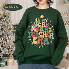 "Custom Christmas Teacher Sweatshirt, In My Very Merry Teacher Era Merry Xmas Teacher Appreciation, winter Teacher Gift, Xmas Gift For Teacher Welcome to QuartzStone Shop! Thank you for choosing us among many other excellent sellers HOW TO ORDER 1. Select the shirt 𝗦𝘁𝘆𝗹𝗲-𝗦𝗶𝘇𝗲 2. Select the shirt color 3. Select the quantity 4. Fill out your personalized information or leave us any note (if any) 5. Click 𝗔𝗗𝗗 𝗧𝗢 𝗖𝗔𝗥𝗧. If you want to buy more than one, please go back to the listing and repeat the steps. \"If you have any question, please send us a message.\" BRAND  If you want a specific brand, please send us a message right after you place the order. Otherwise, we will send you the t-shirt according to what we have in stock. SIZE CHART We suggest you choose the size you usu Christmas Sweater With Letter Print And Long Sleeves, Christmas Long Sleeve Sweater With Letter Print, Green Winter Sweater With Letter Print, Green Letter Print Sweater For Winter, Green Letter Print Tops For Winter, Letter Print Sweatshirt Winter Gift, Christmas Long Sleeve Sweatshirt With Letter Print, Christmas Sweater With Letter Print, Green Letter Print Sweatshirt For Winter