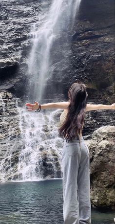 a woman standing in front of a waterfall with her arms outstretched out to the side