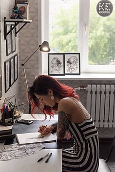 a woman with red hair sitting at a desk writing on a piece of white paper