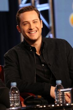 a smiling man sitting at a table with water bottles