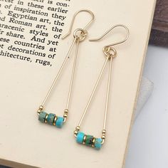 "These Gold and Turquoise Triangle Dangle Earrings are perfect for adding a unique twist to your look! The gold and turquoise jasper combo give these statement earrings a boho-chic style that's sure to wow. An eye-catching look that's as bold as you are! * .14k Gold Filled Wire * Measure approximately 2.5\" from top of ear wire * Stunning turquoise jasper heishi style beads * Sent in a Ribboned Gift Box with Polishing Cloth * Handmade in Montana   ----- OUR MATERIALS -----  *STERLING SILVER - Ex Minimalist Turquoise Wire Wrapped Earrings, Modern Gold Earrings, Gold Triangle, Earrings Turquoise, Ear Rings, Handmade Gold, Etsy Earrings Dangle, Gold Earrings Dangle, Dainty Earrings