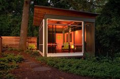 a small house in the middle of some trees and bushes, with a patio area on one side