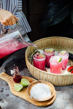 a woman pours water into glasses filled with fruit and limeade on a tray