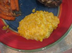 a red plate topped with meat and veggies next to carrots on a counter