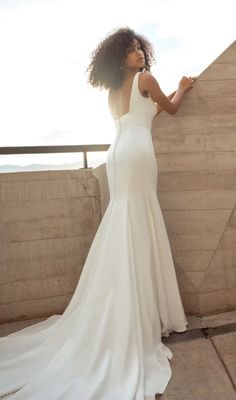 a woman in a white dress leaning against a wall with her hand on the side