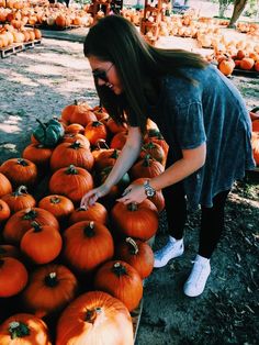 a woman is picking up pumpkins from a cart at a pumpkin patch with lots of other pumpkins in the background