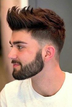 a young man with a beard and long hair wearing a white t - shirt is looking at the camera