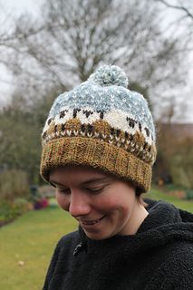 a young man wearing a knitted hat and looking at his cell phone in the park