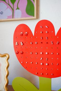 a red heart shaped object sitting on top of a wooden table next to a vase