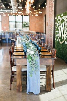 a long table with blue linens and white flowers on it is surrounded by wooden chairs