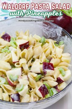 pasta salad with pineapples and cherries in a glass bowl next to an apple