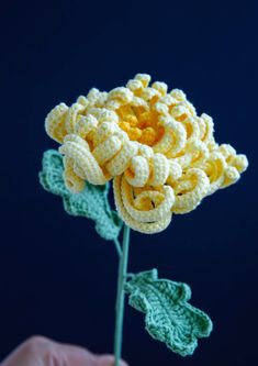 a crocheted yellow flower with green leaves in the foreground, against a dark blue background