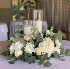 white flowers and greenery sit on a table with candles in the centerpieces