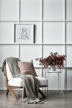 a white chair sitting in front of a wall with pictures on it and a potted plant