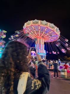 a woman taking a photo with her cell phone in front of a carousel at night