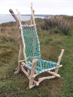 a chair made out of sticks and rope on top of a grass covered hill next to the ocean