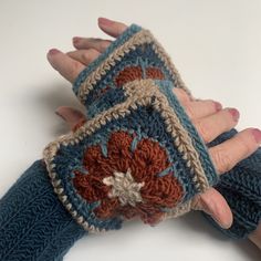 a woman's hand is holding two crocheted gloves with flowers on them