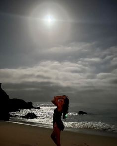 a woman standing on top of a beach next to the ocean under a cloudy sky