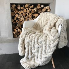 a white chair sitting in front of a fire place covered in a cable knit blanket