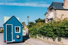 a tiny blue house sitting on the side of a road next to a brick building