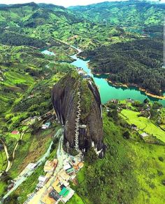 an aerial view of a large mountain with green fields and trees around it, surrounded by water