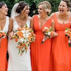 a group of women standing next to each other wearing orange dresses and holding bouquets