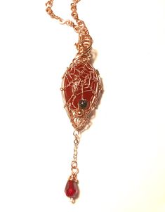 a red and gold necklace with an intricate design on the front, hanging from a golden chain