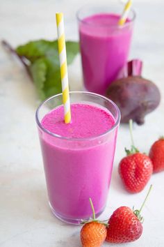 two glasses filled with pink smoothie next to strawberries and beets on a table