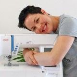 a man is smiling while working on a sewing machine with flowers in front of him