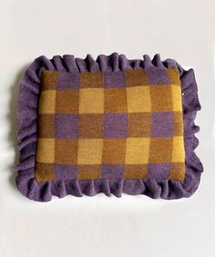 a purple and yellow checkered pillow with ruffles on the bottom, sitting on a white surface