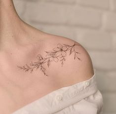 a woman with a flower tattoo on her left shoulder and right shoulder is wearing a white shirt