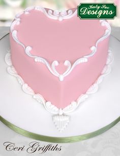 a pink heart shaped cake sitting on top of a white platter with green lettering