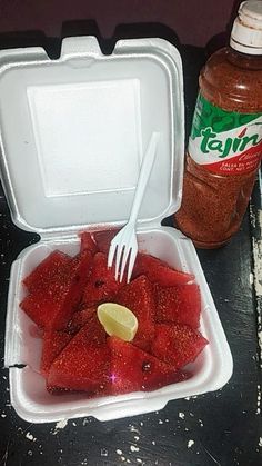 a plastic container filled with strawberries next to a bottle of ketchup and a fork