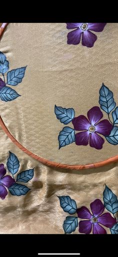 an embroidered cloth with purple flowers and leaves on it, as well as a leather hoop