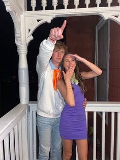 a man and woman standing on a porch pointing at something with their fingers in the air