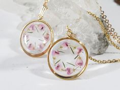 two necklaces with pink flowers on them sitting next to a piece of crystal rock