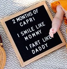 a baby laying next to a sign that says 2 months of capri i smile like mommy i fart like daddy