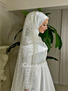 a woman wearing a white veil and dress with beading on the skirt is standing in front of a potted plant