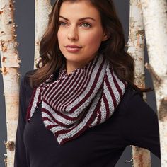 a woman standing in front of some trees wearing a striped knitted scarf and black top