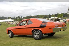 an orange muscle car parked on top of a grass covered field next to other cars