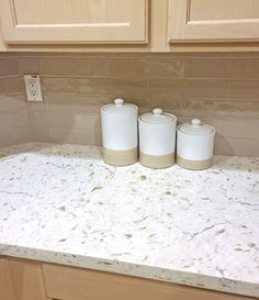 three white canisters sitting on top of a marble countertop in a kitchen