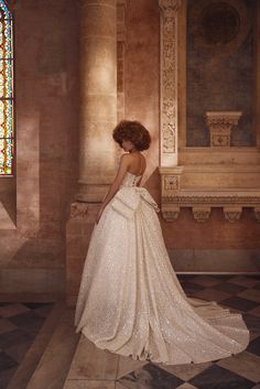 a woman in a wedding dress looking at the stained glass window behind her is a bench