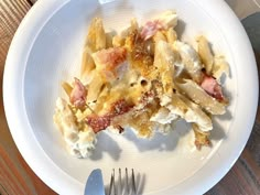 a white plate topped with pasta covered in cheese and bacon next to a silver fork