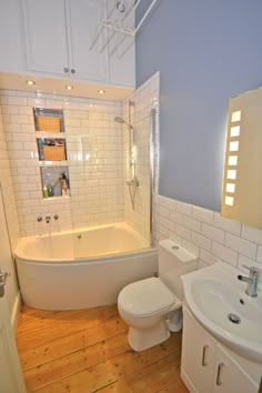 a white toilet sitting next to a bath tub in a bathroom on top of a hard wood floor