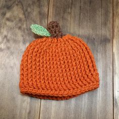 an orange knitted pumpkin hat with a green leaf on the top sits on a wooden surface