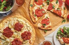 two pizzas sitting on top of brown paper next to cups of tea and sauce