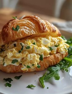 an egg salad sandwich on a croissant with fresh greens and parmesan cheese