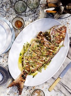 a white plate topped with fish on top of a table next to glasses and utensils